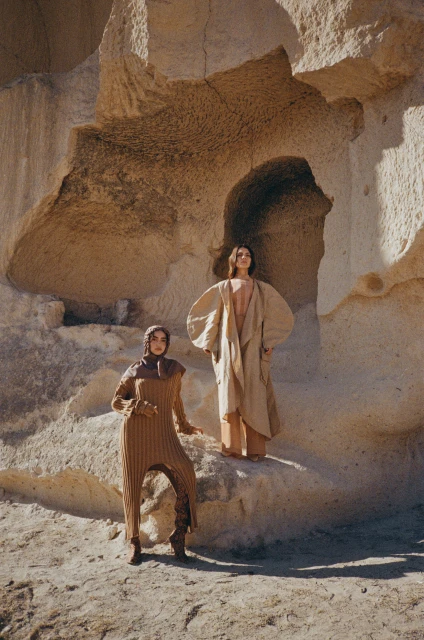 Two women in tan outfits pose near a unique sandstone rock formation in an outdoor fashion editorial, showcasing minimalist desert style.