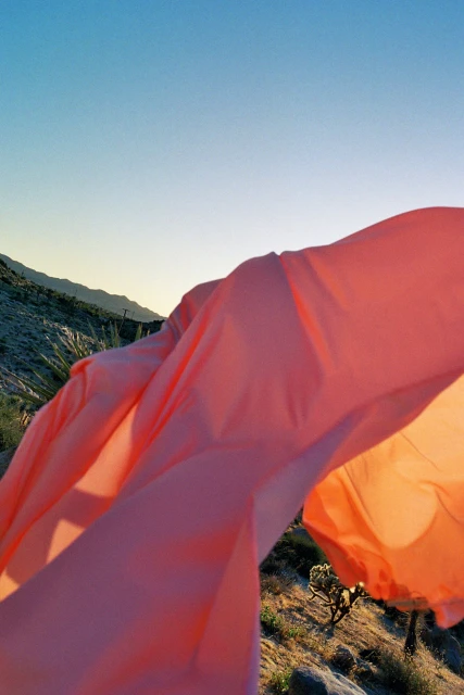 Peach fabric billows in a desert landscape with mountains under a clear blue sky creating a soft, dreamy outdoor editorial.