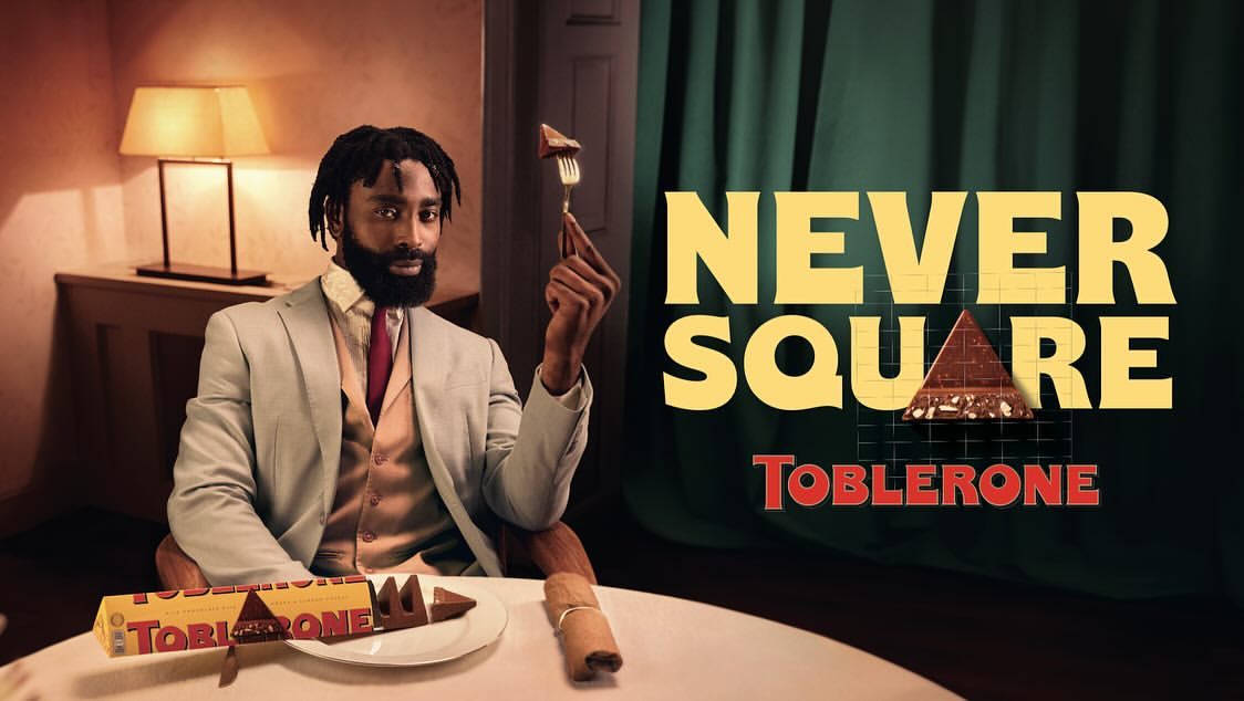 Indoor shot of an African-American male model wearing a suit and holding a piece of chocolate on a fork, with chocolate bar.