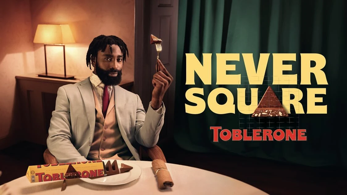 Indoor shot of an African-American male model wearing a suit and holding a piece of chocolate on a fork, with chocolate bar.