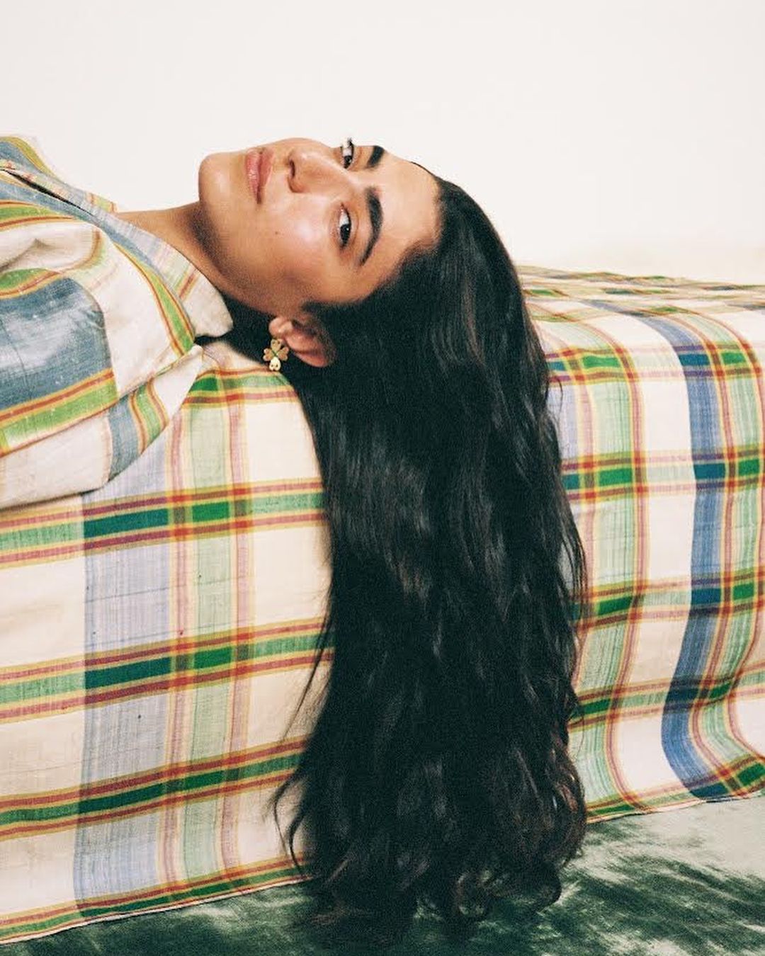 Portrait of a woman laying on a patterned surface, featuring long dark hair, earrings, and wearing a striped shirt.
