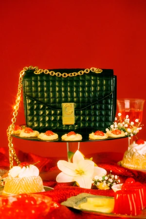 Elevated view of a black purse with a gold chain on a dessert table with jello, cookies, and flowers against a vibrant red backdrop.