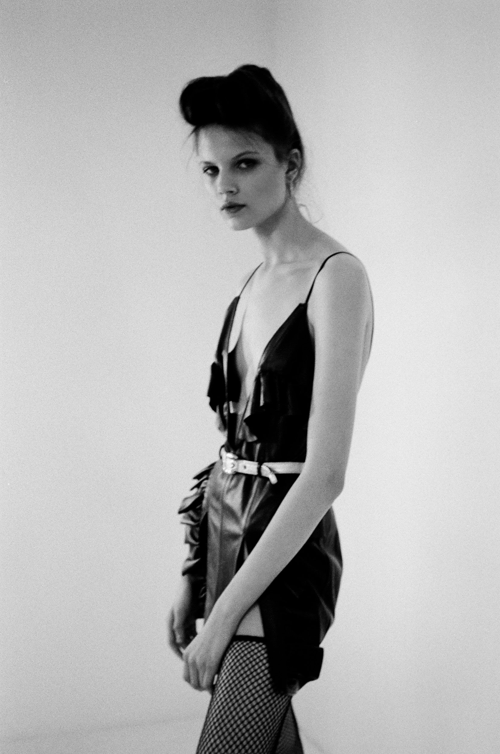 Monochrome portrait of a woman in a dark slip dress and fishnet tights against a plain background