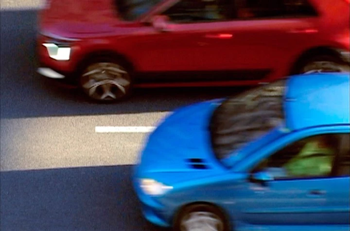 High-angle view of a red SUV and a blue compact car moving on an asphalt road surface with lane markings; motion blur is present.
