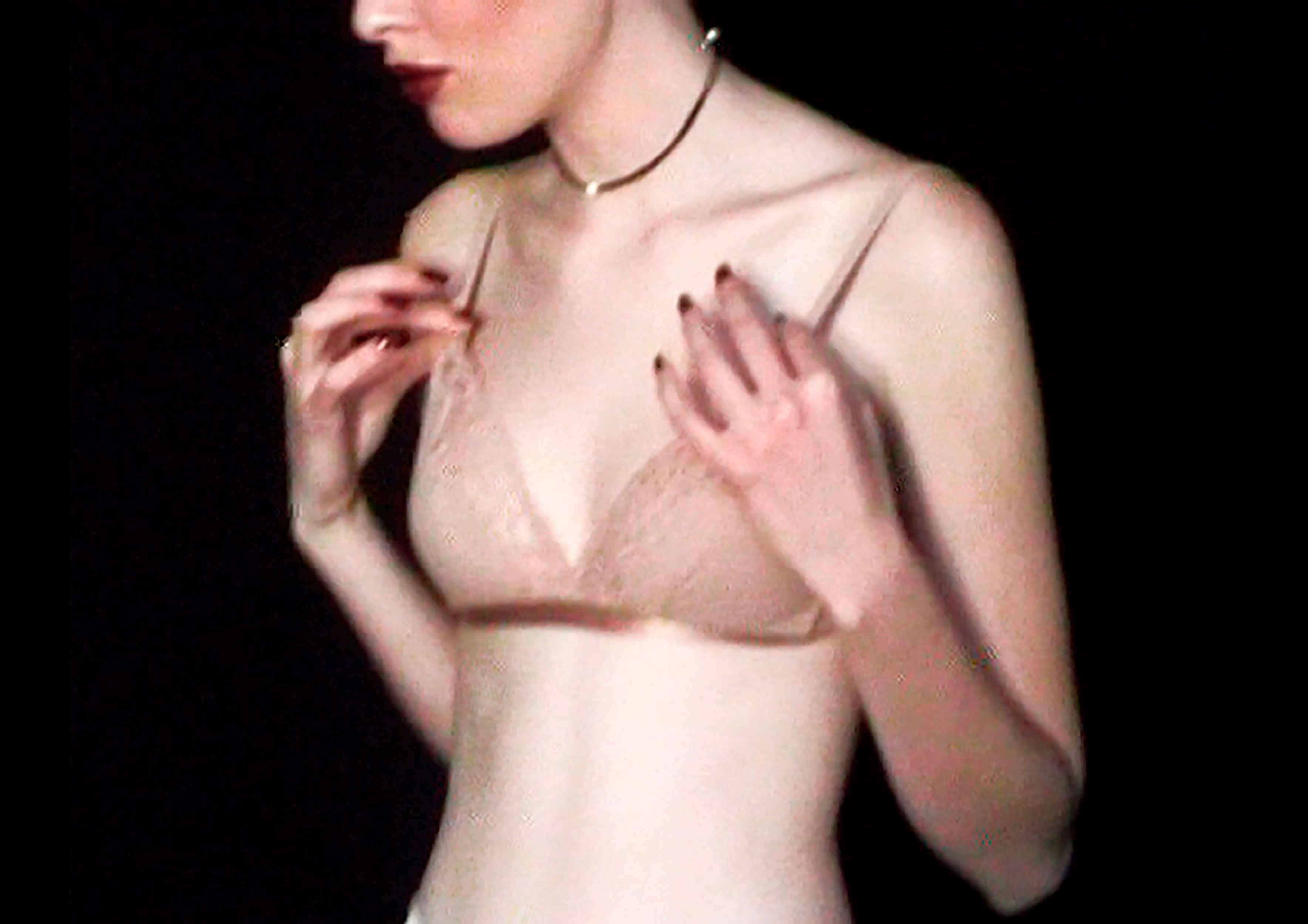 Close-up of a fair-skinned adult female adjusting the strap of a lace bra against a dark background. Red lipstick is visible.