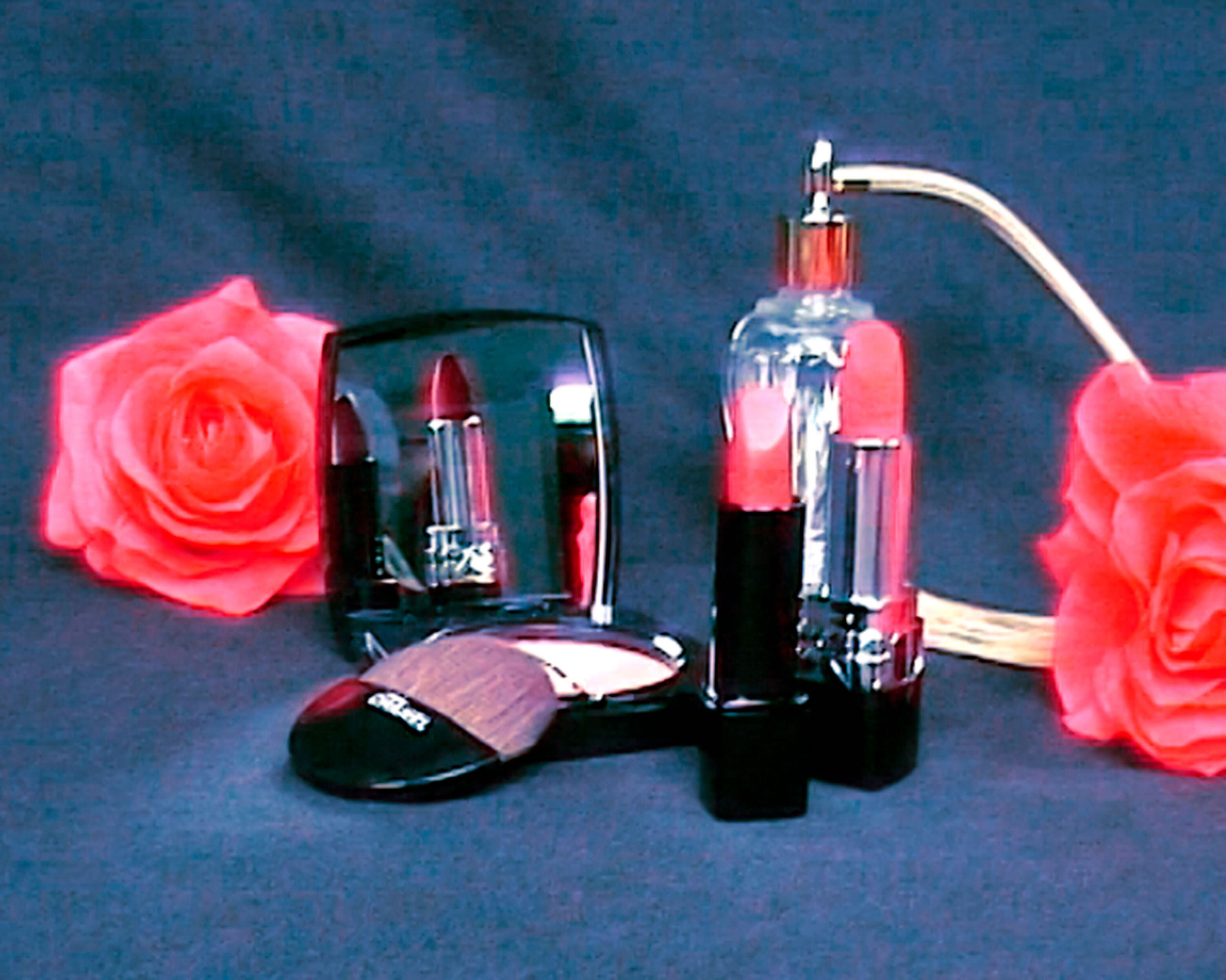 Cosmetics layout featuring two tubes of lipstick, a compact mirror with powder brush, a perfume bottle, and vibrant red roses.