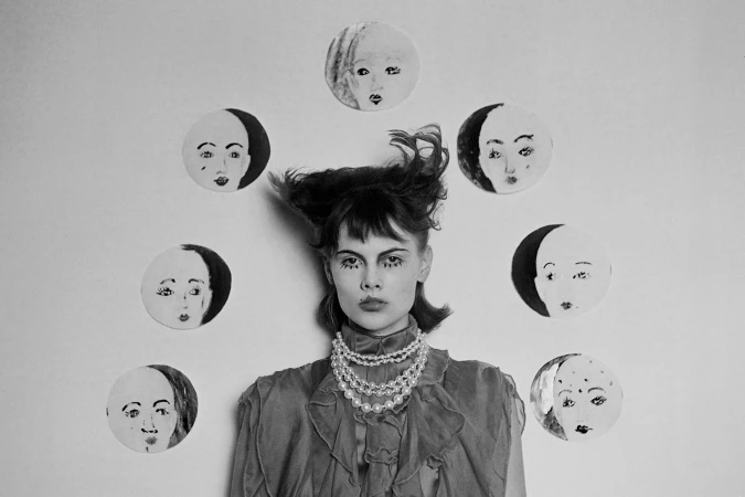 Artistic black and white portrait of a woman with creative makeup and hair, surrounded by circular paper portraits against a light background.