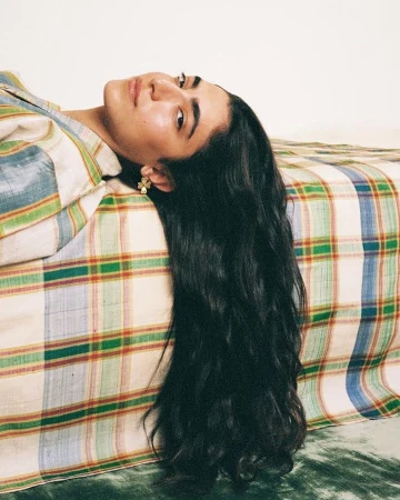 Woman with long dark hair lying on a plaid patterned bed, photographed by Mar Ordonez.