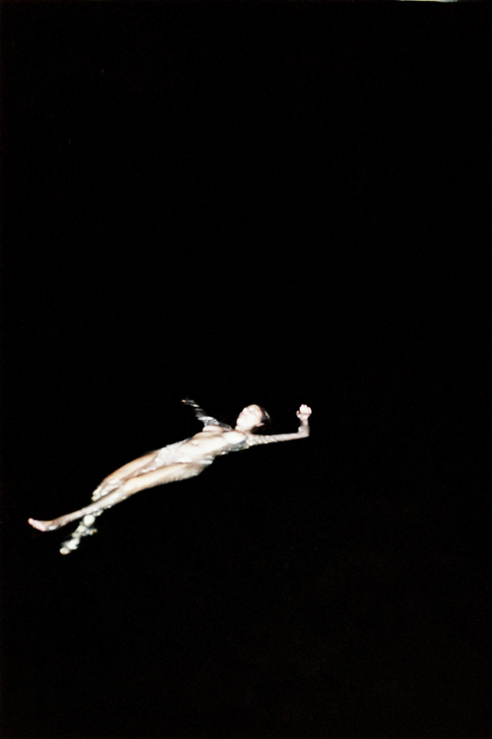 Artistic photograph of a female figure in an aquatic pose against a stark black background, creating a striking contrast and ethereal effect.