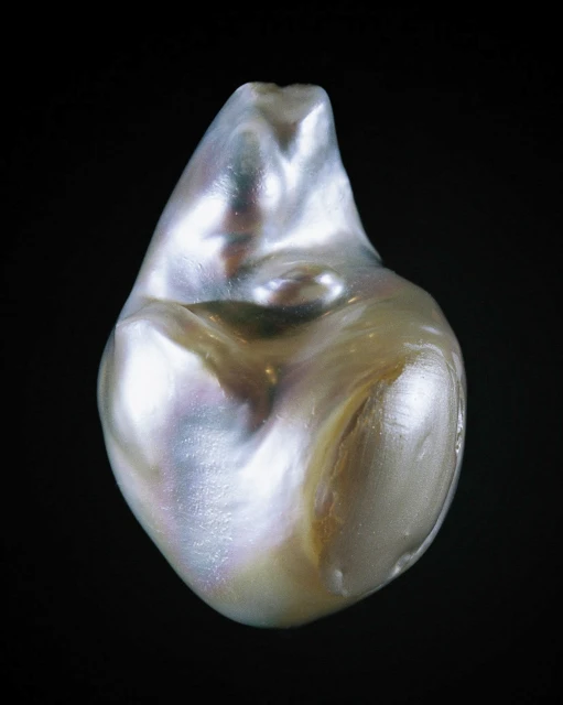 Close-up of a lustrous, baroque pearl with iridescent tones against a dark background, highlighting its unique shape and texture.