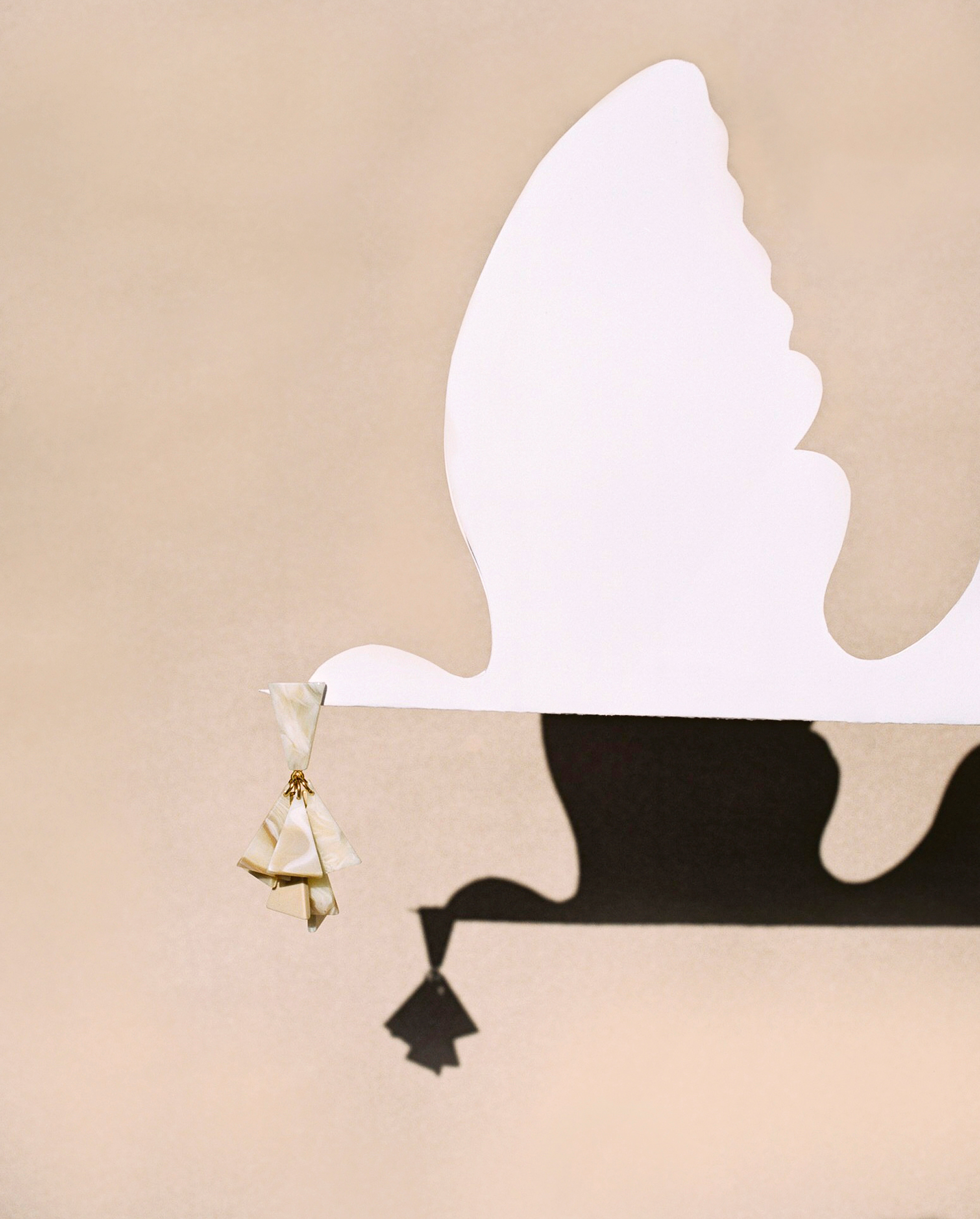 Abstract, geometric composition featuring a white, dove-shaped cut-out, decorative object with origami-like elements against a neutral background.