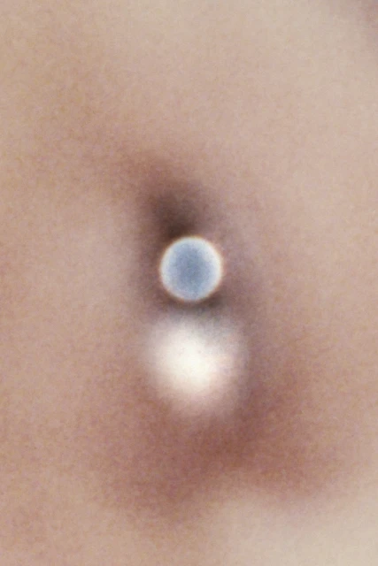 Close-up of a person's pierced navel. A silver ball is visible where a piercing would be located, with the person's skin in the background.