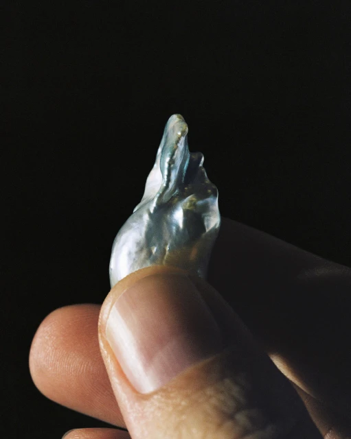 Hand holds baroque pearl with iridescent shimmer against a dark background, close-up studio shot for jewelry or fashion.