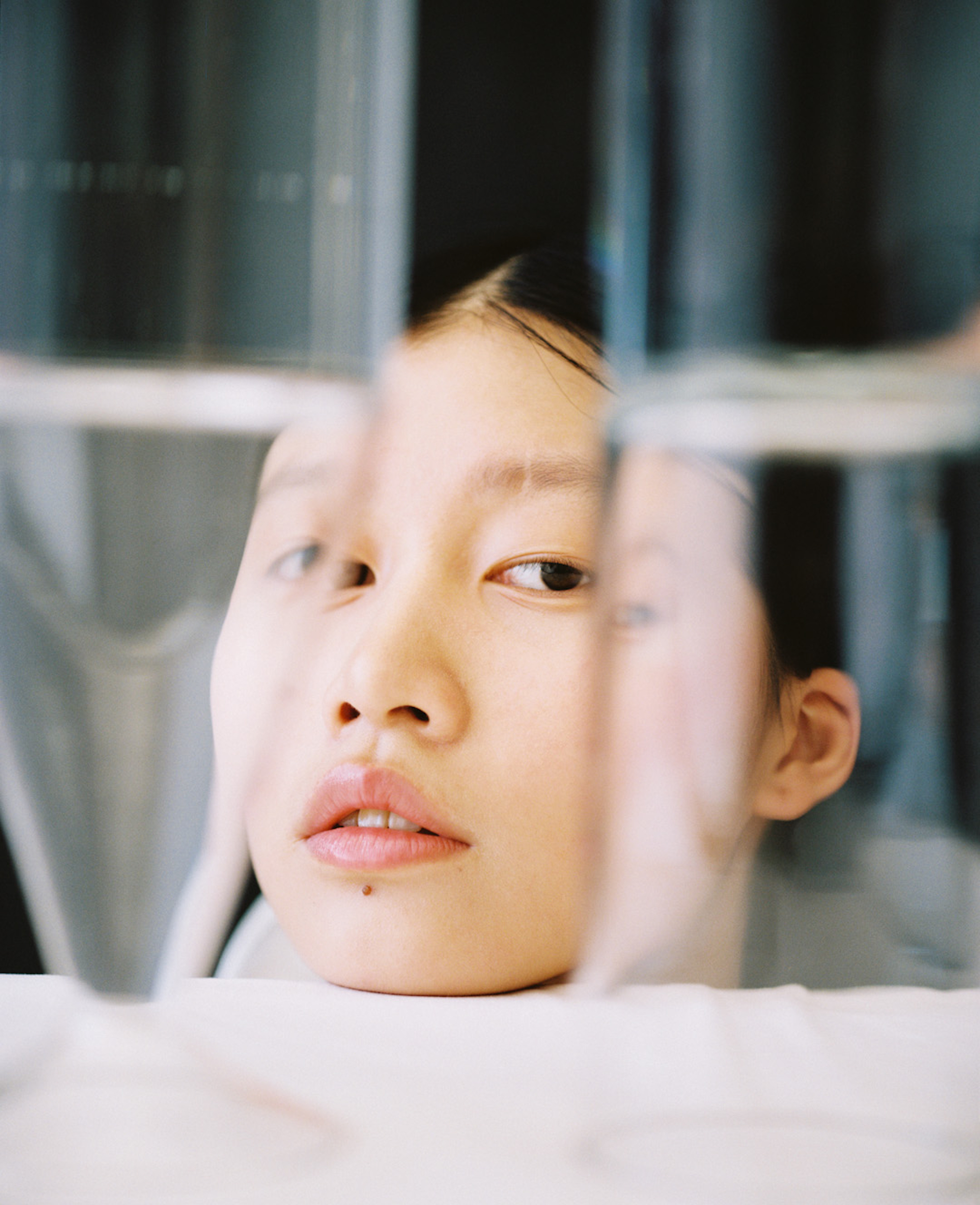 Close-up studio shot of an Asian young adult woman looking at the camera through clear glass panels creating distortions.