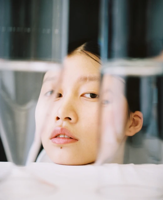 Close-up studio shot of an Asian young adult woman looking at the camera through clear glass panels creating distortions.
