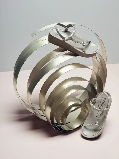 Elevated shot of platform sandals arranged alongside a metal sculpture, set against a two-tone grey and light pink background.