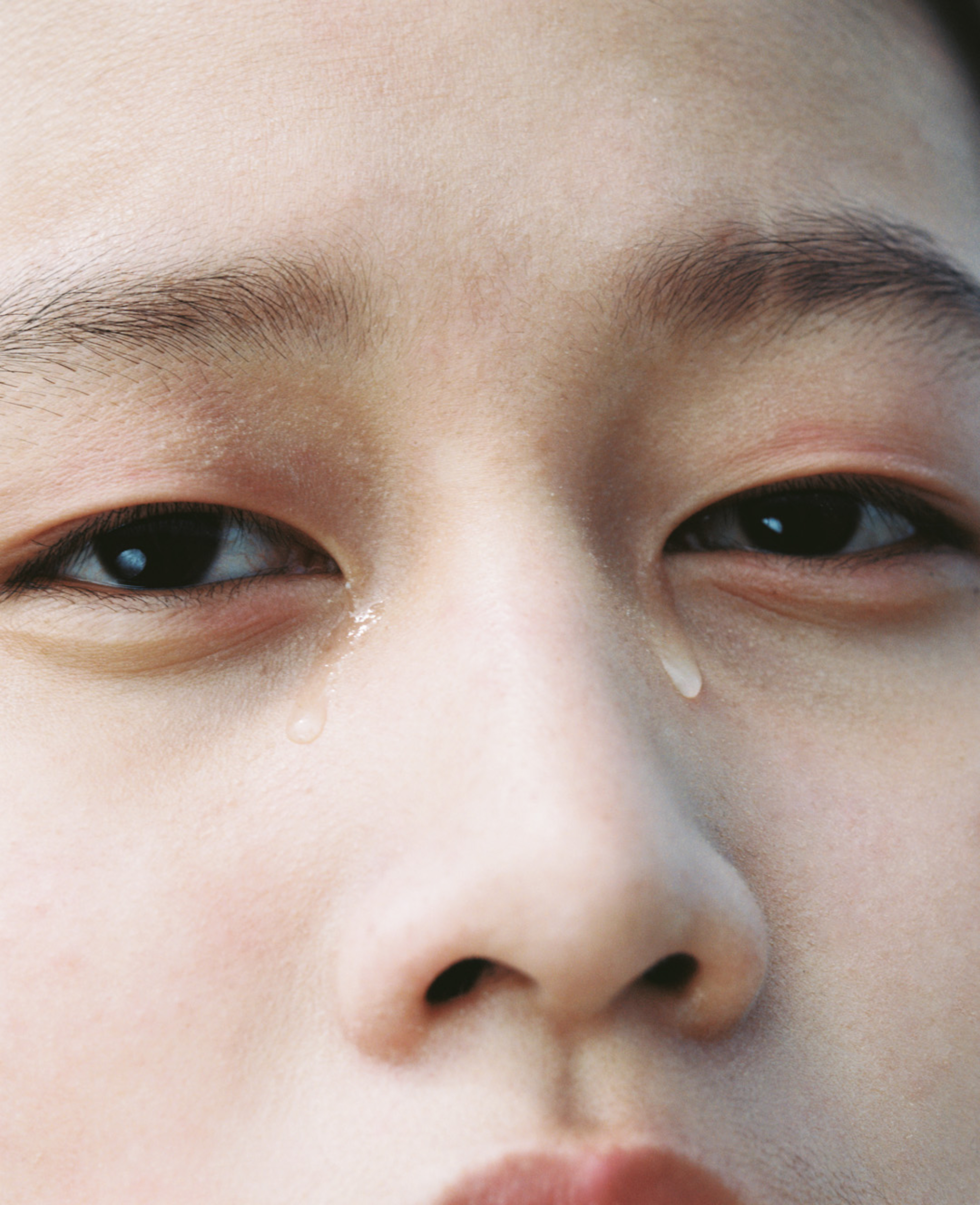 Close-up shot of a young adult's face with tears visible. The focus is on the individual's eyes and the single tear on their cheek.