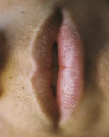 Close-up of human lips with lipstick, emphasizing texture and detail in a minimalist composition. The image highlights natural skin tones.