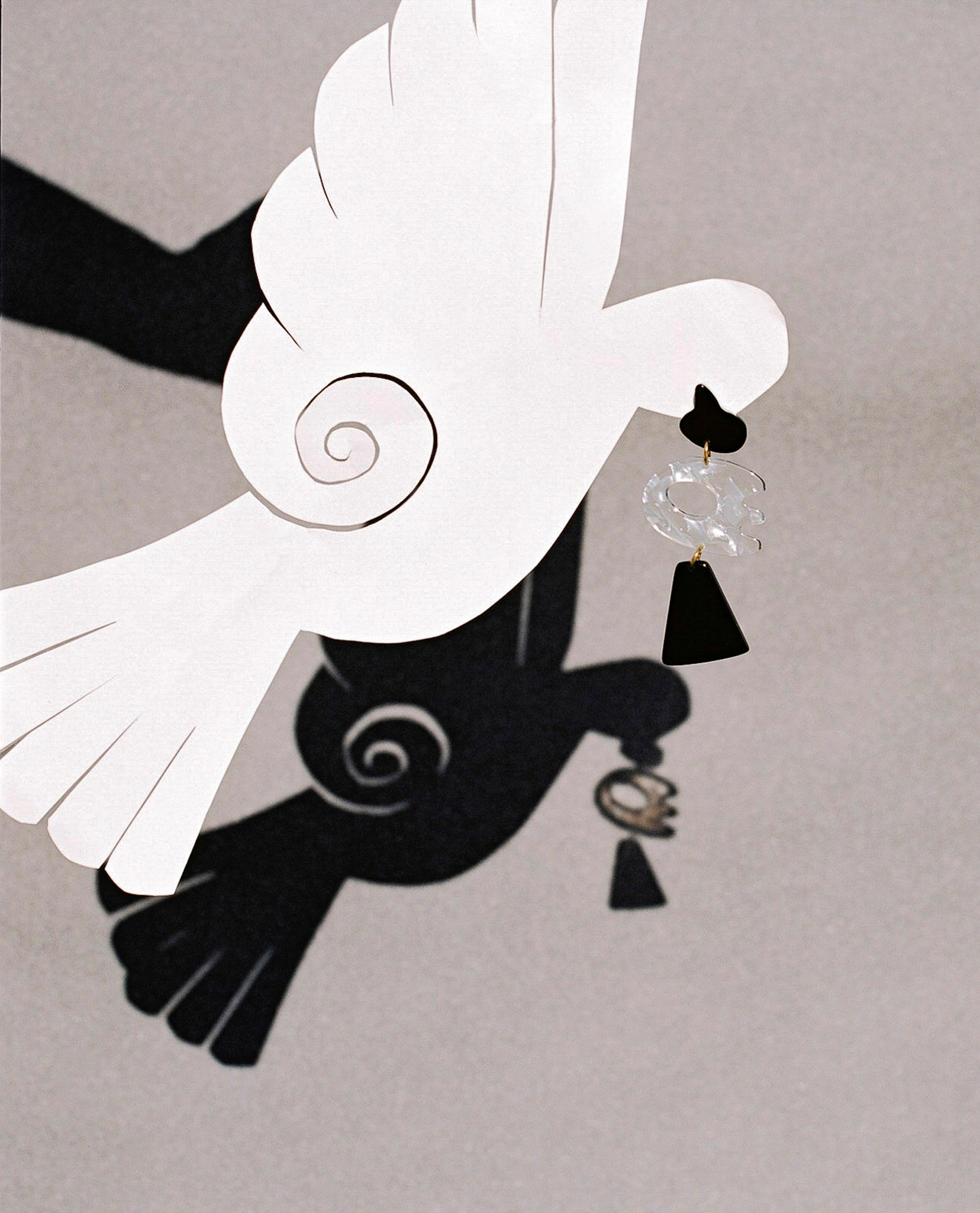 Abstract-shaped earrings on a white and black cut-out dove against a light gray background create a graphic jewelry display.
