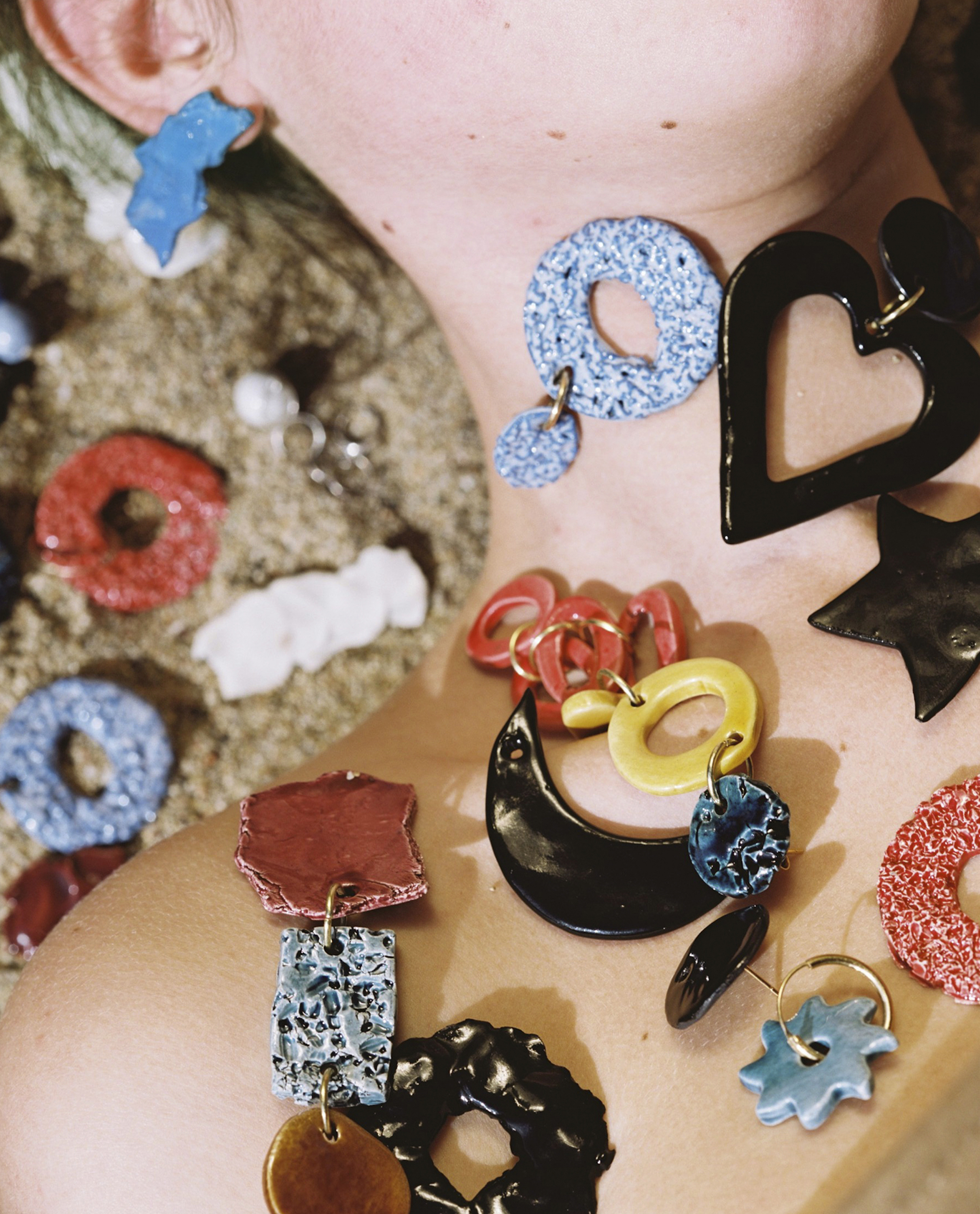 Abstract jewellery pieces displayed on a person's skin. The earrings and necklaces have organic shapes and a mix of textures and colors.