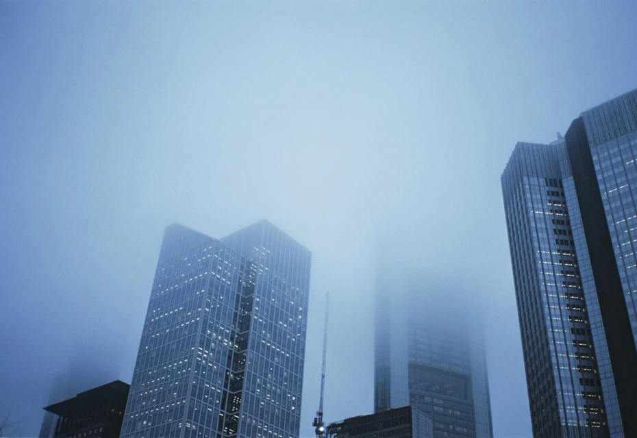 Low-angle view of skyscrapers disappearing into dense fog, creating a sense of mystery and urban atmosphere in a city setting.