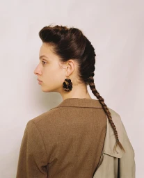 Profile portrait of a young woman with a braided hairstyle wearing tortoiseshell earrings and a brown jacket by Rita Puig-serra Costa