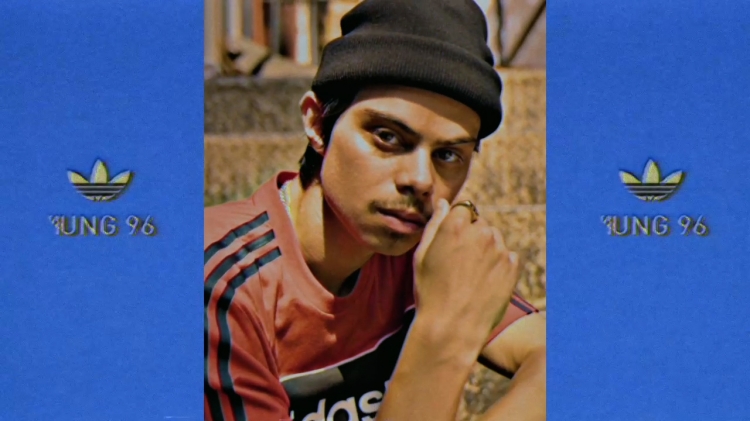 A young adult poses with a beanie and Adidas apparel against a blue backdrop, creating a casual yet stylish portrait.