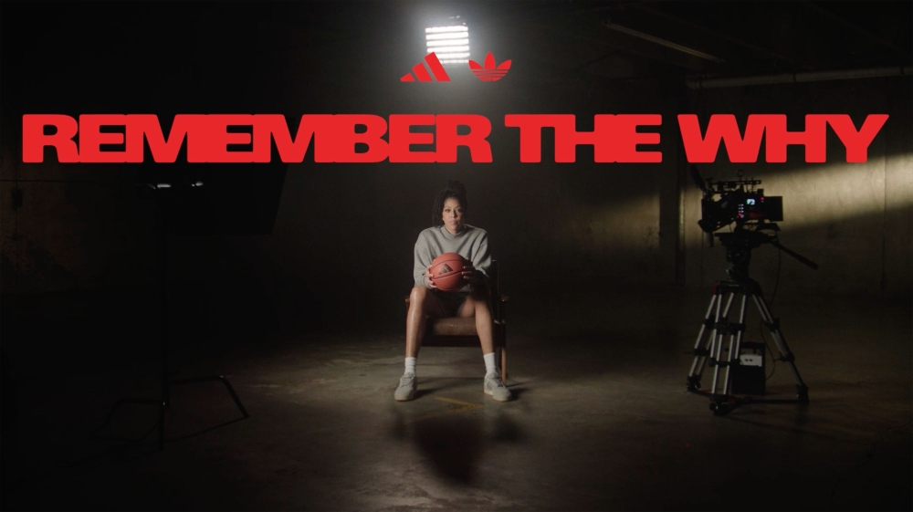 Adult female basketball player sits in dark studio with basketball and Adidas logo. Camera faces the woman with bright lighting.