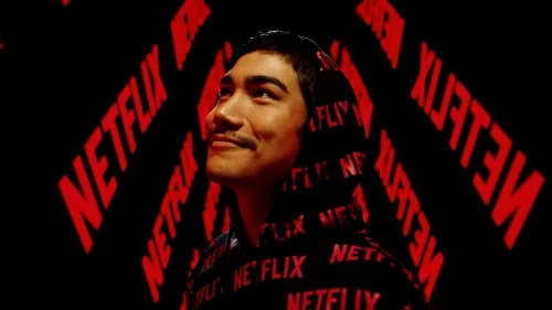 Portrait of a young adult male with a slight smile wearing a Netflix-branded hoodie against a background with the Netflix logo.