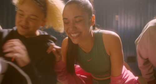 Group of diverse smiling women in sportswear in an indoor setting, suggesting fitness, sports, or active lifestyle themes. 