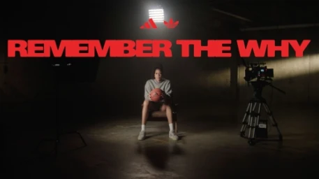 Woman seated on chair holding a basketball in a dimly lit industrial space with film equipment and red typographic overlay