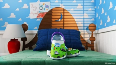 Green clogs with decorative charms placed centrally on a green bed in a room with blue cloud-patterned wallpaper.