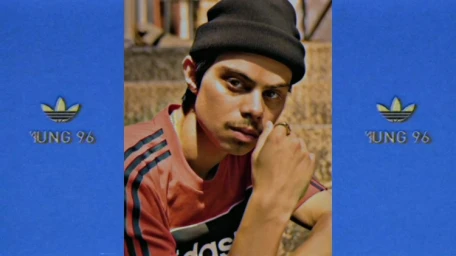 Close-up portrait of a man wearing a black beanie and an orange and black t-shirt against a textured blue frame.