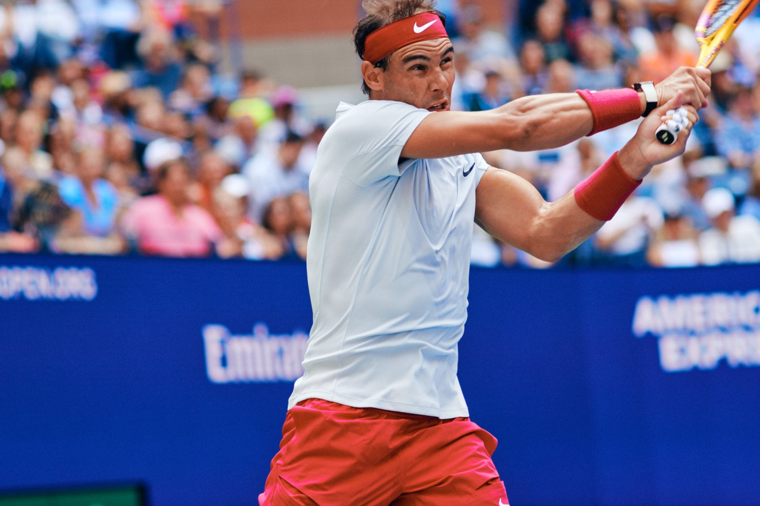 Athlete in action at a tennis match, striking the ball with a racket. An outdoor sporting event with an audience in the background.