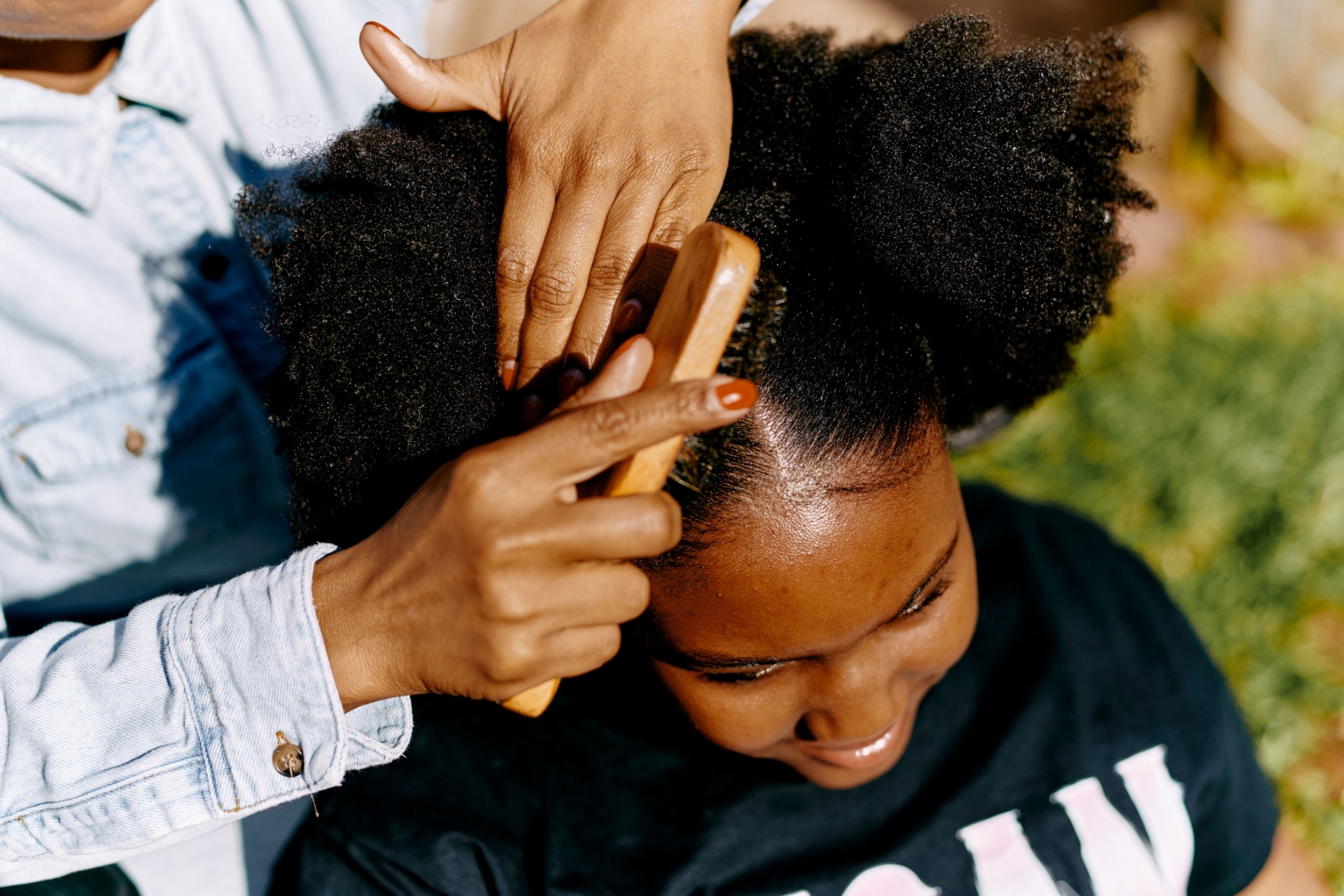 Close-up of hands brushing an African American female's hair outdoors, emphasizing beauty, hair care, natural hair, and personal grooming.