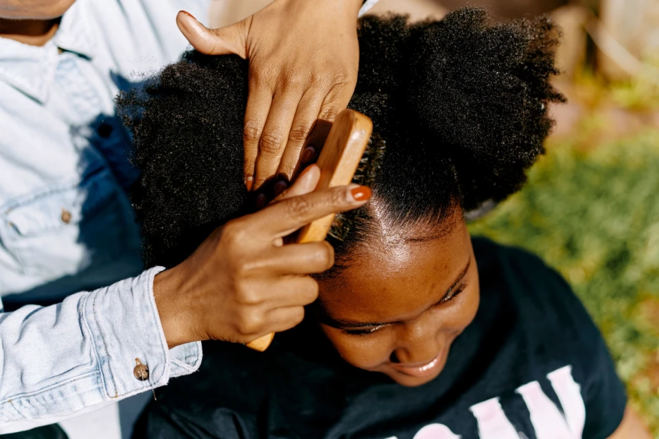 Close-up of hands brushing an African American female's hair outdoors, emphasizing beauty, hair care, natural hair, and personal grooming.