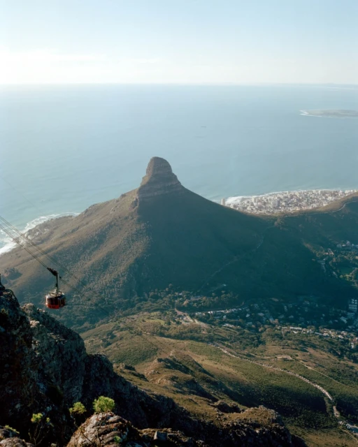 Aerial view of Table Mountain and Lion's Head, South Africa, with a cable car ascending, showing scenic coastline and natural beauty.