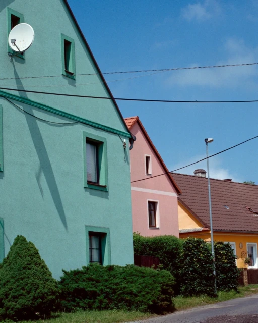 A row of colorful houses beneath a bright blue sky with scattered clouds, creating a cheerful suburban scene on a sunny day.