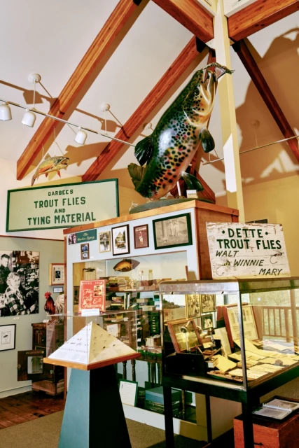 Interior view of a museum display featuring a large trout sculpture, vintage signage, and various artifacts related to fly fishing.