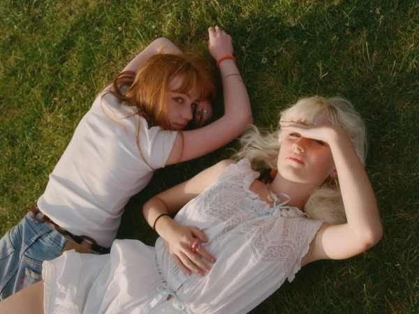 Two young women with red and blonde hair lying on green grass outdoors in a high angle portrait shot by Ana Cuba.