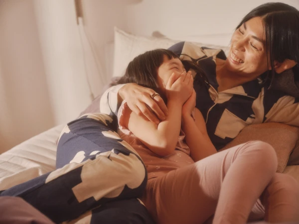 Woman and child laughing together while lying in bed wearing patterned pajamas, captured in soft warm light
