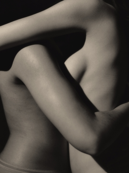 Striking monochrome photograph of two nude figures intertwined, showcasing the beauty of human form through light and shadow.
