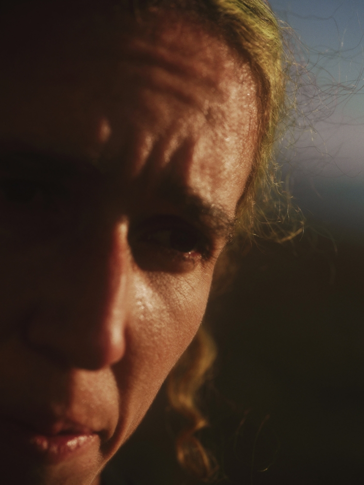 Close-up of an adult with golden curly hair, deep shadows, and minimal detail, offering an intimate and intense portrait.