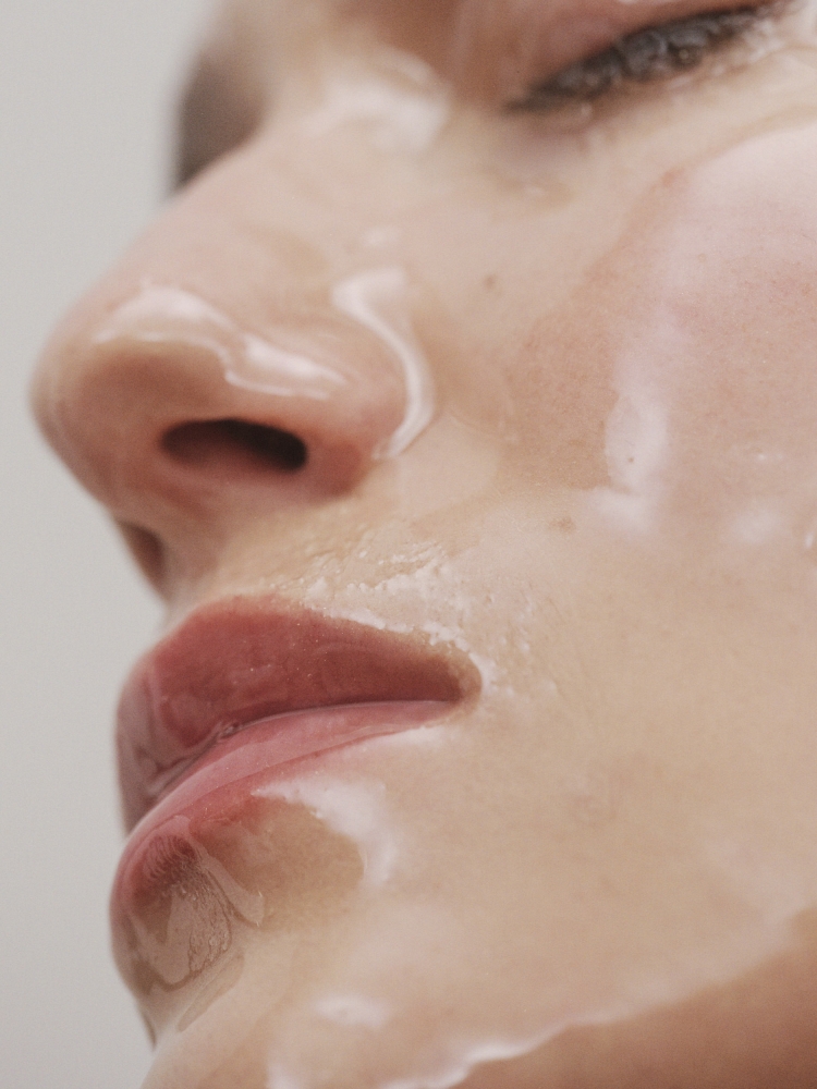 Close-up shot of a person's face with a glossy, translucent substance, possibly a skincare product, highlighting skin texture and contours.