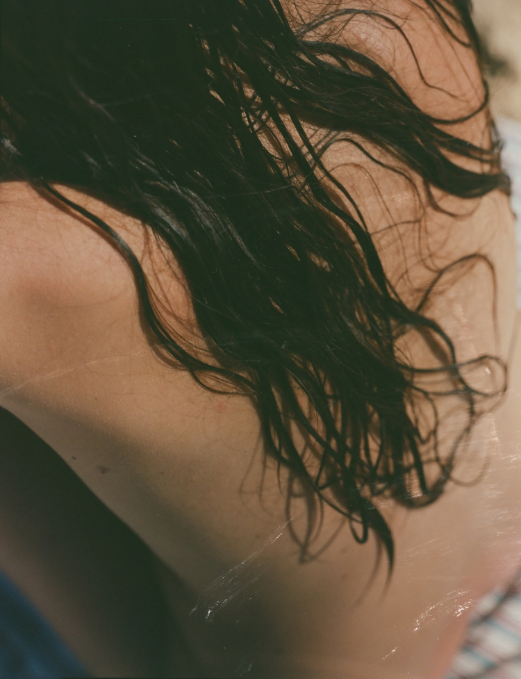 Close-up portrait of a person with wet dark hair draped across their bare back, photographed by Ana Cuba
