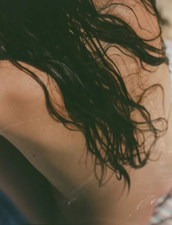 Close-up portrait of a person with wet dark hair draped across their bare back, photographed by Ana Cuba