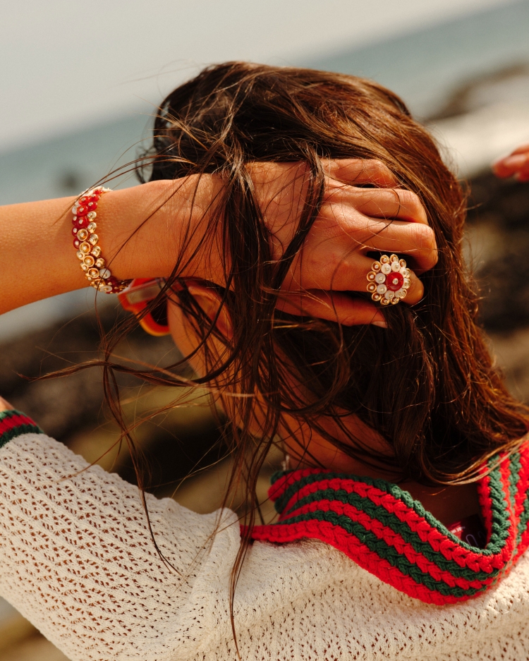 Woman wearing a ring and bracelet poses on a rocky beach with the ocean in the background in an outdoor shot.