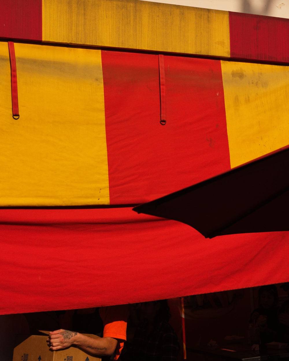 Striped red and yellow awning with an adult pointing to a cardboard box in a low-angle medium shot in outdoor setting.