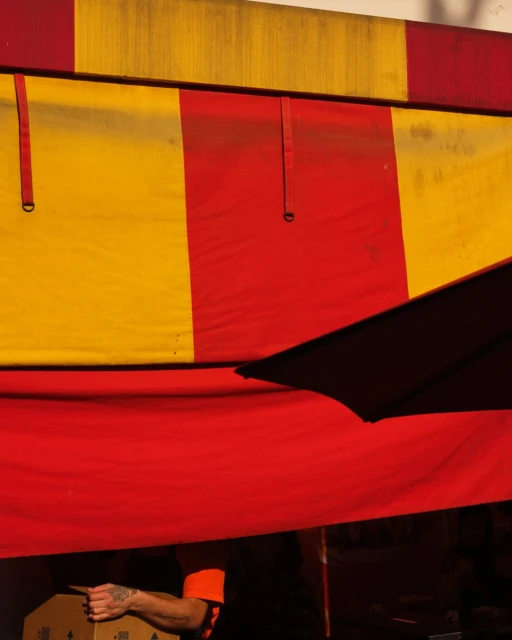 Striped red and yellow awning with an adult pointing to a cardboard box in a low-angle medium shot in outdoor setting.