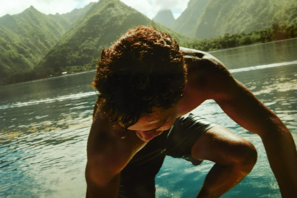 Adult male in black swim trunks in turquoise water, mountains in the background, sunny day with natural lighting.